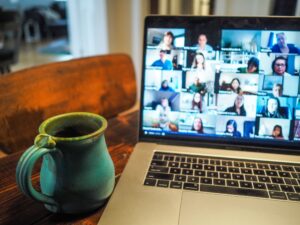 Mug to the left of a laptop with people on a virtual platform.